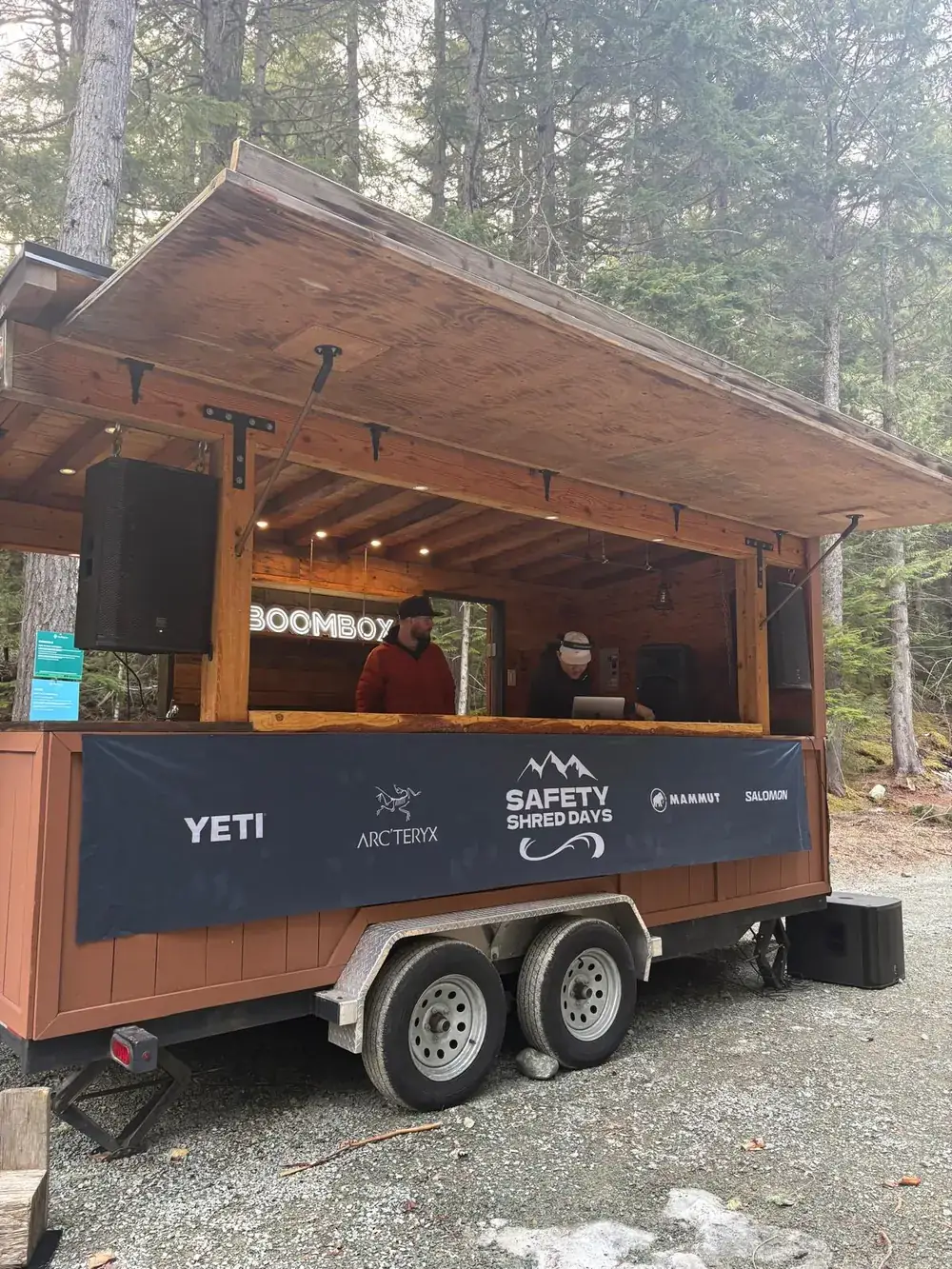 Two DJs in the Whistler Boombox booth above the Safety Shred Days sponsor banner