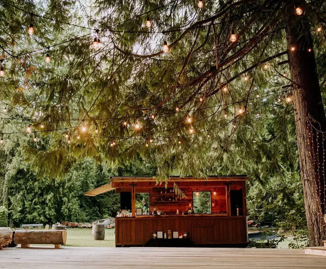 Douglas fir timber mobile bar trailer in a forest clearing under string lights near Whistler