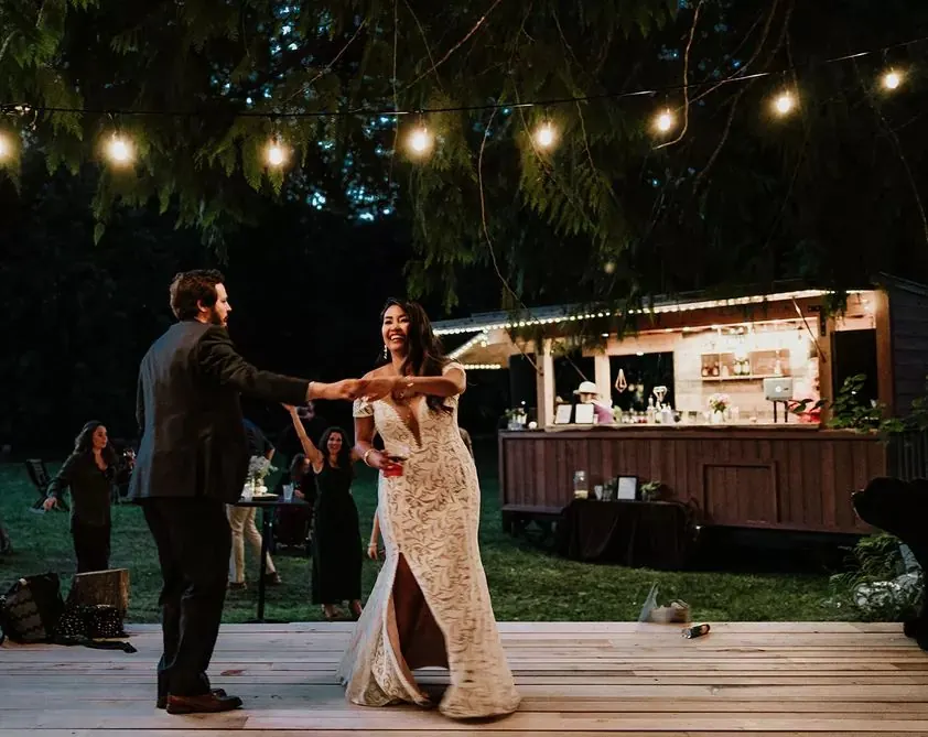 First dance on a wooden deck under string lights with the Boombox bar behind